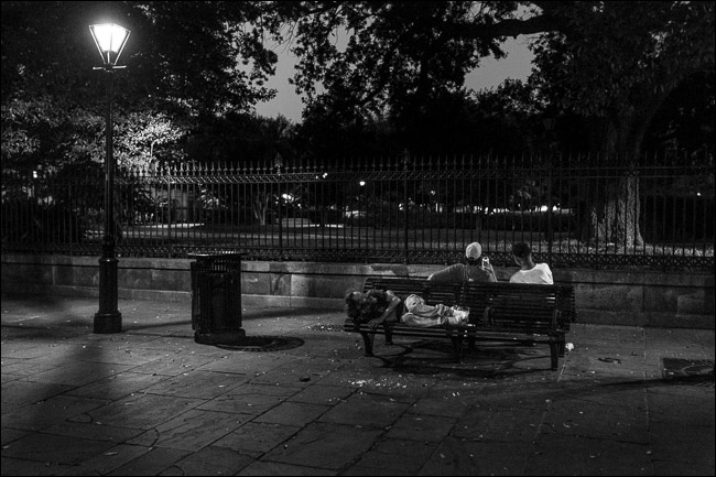 due uomini seduti sulla panchina del parco di notte;  un uomo che dorme sul sedile dietro di loro
