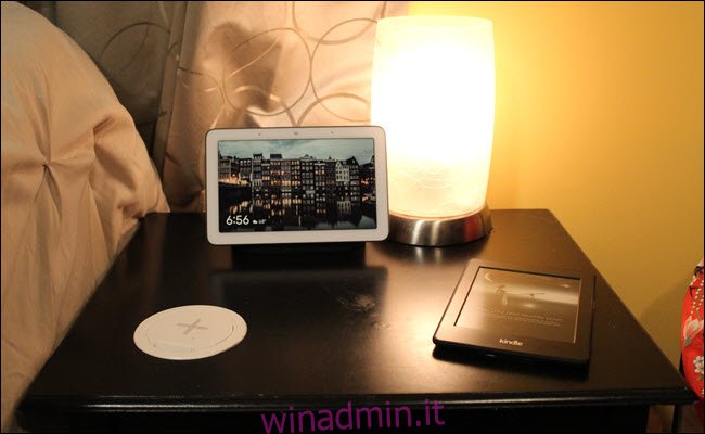 Un comodino con un caricabatterie wireless posizionato sulla superficie, un kindle e Google Home Hub