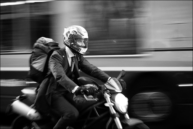 uomo in tuta in sella a una moto con autobus sfocato in movimento dietro di lui