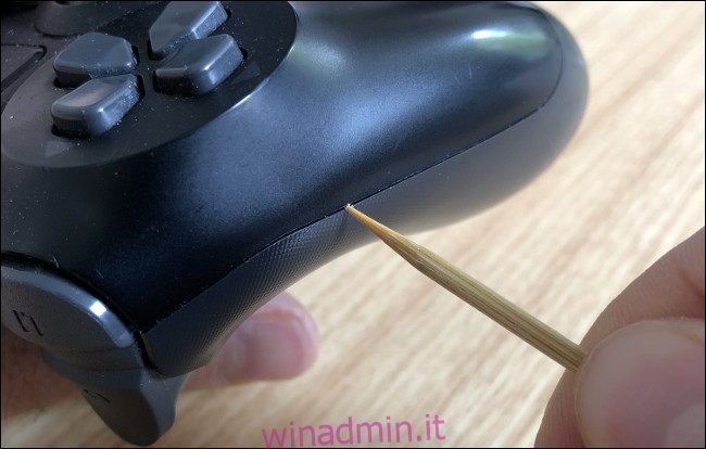 Una mano che pulisce una fessura sul lato di un DualShock 4 con uno stuzzicadenti.