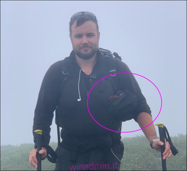 Un uomo che cammina sotto la pioggia portando un treppiede e una borsa Shell per fotocamera Peak Design.