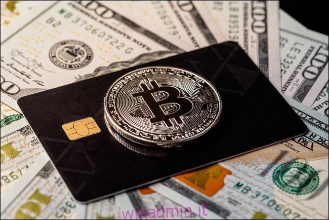 Un token Bitcoin fisico sopra una carta di credito che giace su banconote da $ 100.